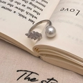 Macro detail of leaf-shaped zircon ring with white pearl on vintage book pages - Silver Peacock Feather Pearl Ring