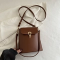 Brown faux leather mini crossbody bag with unique gold hardware on soft fabric background - Brown