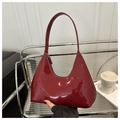 Primer plano de un bolso de charol burdeos con forma de media luna y acabado brillante - Rojo