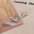 Détail de boucles d'oreilles nœud argentées sur un fond de toile crème minimaliste - Boucles d'Oreilles Clous Nœud de Base en Métal Poli Argentées (A-904)