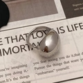 Primo piano di un anello in metallo liquido argento lucido su un giornale - Anello Aperto Argentato a Superficie Liscia Grande