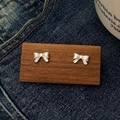 Detailansicht der silbernen Schleifen-Ohrstecker auf dunklem Holz und Denim-Stoff - Silber