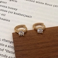Détail macro de créoles dorées avec un zircon étincelant sur un socle en bois - Boucles d'oreilles en zircon blanc doré