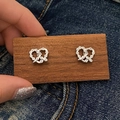 Detail von silbernen Brezel-Ohrsteckern mit Zirkonia-Besatz auf Denim-Hintergrund - Silber