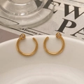 Detailansicht goldener C-Ohrringe mit zirkonbesetzten Kugeln auf weißer Keramikschale - C-Form Ohrstecker / Gold