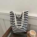 Striped canvas tote bag with dual handles shown on a wooden table in a minimalist setting - Black and White Horizontal Stripes / Black