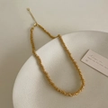 Détail d'un collier de perles dorées à texture spirale sur une assiette en céramique - Doré
