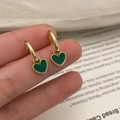 Detailopname van groene hartvormige oorbellen met gouden parelrand in warme setting - Groene Hart Oorbellen