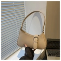 Detalle de bolso baguette de cuero beige con hebilla plateada frente a una ventana suave - Caqui