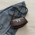 Bolso de hombro marrón oscuro con lazo plateado sobre fondo de chaqueta vaquera - Marrón