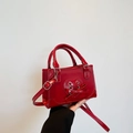Glossy red faux leather handbag featuring a heart-shaped bow and adjustable shoulder strap - Red