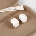 Macro detail of silver oval enamel stud earrings on a textured handmade gift box - White