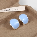 Detailed close-up of sky blue enamel oval stud earrings on a textured craft tray - Blue