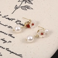 Dettaglio di orecchini a fiore vintage con perla e gemma rossa su sfondo di lino - Fiore Rosso