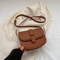 Borsa a sella in pelle marrone caramello con patta e tracolla sottile su bianco - Cuoio