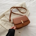 Borsa a tracolla in pelle marrone caramello con fibbia dorata su sfondo beige - Marrone