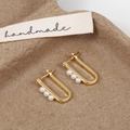 Gros plan sur les boucles d'oreilles dorées en U avec perles sur fond cartonné - Doré