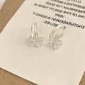 Primer plano de pendientes de flores plateados con circonitas en tarjeta blanca - Plateado
