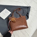 Caramel brown leather tote bag with long straps and a plush puppy charm on a white fabric - Brown with Pendant