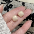 Minimalist square rounded pearl stud earrings held between fingers for size reference - White