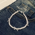 Detalle de una pulsera de perlas con lazos plateados y cierre de mosquetón en mezclilla - Pulsera de Lazo Blanco