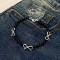 Detalle de una pulsera de perlas negras con tres colgantes de lazo plateado en denim - Pulsera de Lazo Negro