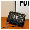 Close-up of quilted black leather bag featuring a silver metal bow buckle and chain strap - Black