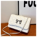 Close-up of white quilted crossbody bag with silver bow clasp and chain strap - White