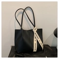 Close-up of black leather tote bag featuring a decorative logo ribbon and sleek texture - Black