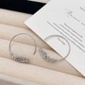 Macro detail of silver C-shaped hoop earrings with intricate wheat leaf relief engraving - Silver