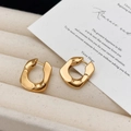 Orecchini a cerchio a U in oro lucido su tessuto beige con un'estetica minimalista - Orecchini a forma di U dorati