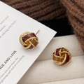 Detalle macro de pendientes retorcidos con esmalte rojo y ámbar sobre tejido de punto - Pendientes de Espiral Bicolores Rojo y Marrón