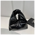 Detail of glossy black pleated PU handbag featuring a signature knotted handle on white stand - Black