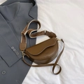 Brown leather saddle bag with dual straps and gold hardware over a grey blazer - Brown