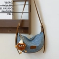 Blue denim half-moon crossbody bag with brown leather strap and plush character charm - With Monster Pendant / Denim Blue