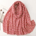 Beige winter scarf with red heart print and gold foil accents shown with lifestyle props - Red