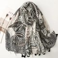 Black and beige scarf with palm leaf prints and tassels laid on a white background - Black