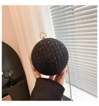Detailed view of black spherical evening bag with golden clasp held in hand for size comparison - Black