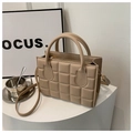 Detalle de un bolso acolchado beige con asas superiores sobre un soporte blanco - Caqui