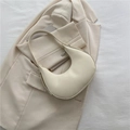 Elegante bolso de media luna color crema en cuero mate liso sobre un blazer a juego - Blanco