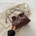 Bolso tipo cubo plisado marrón oscuro con cadena plateada sobre una chaqueta beige - Marrón