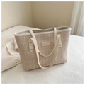 Close-up of beige woven straw tote bag featuring cream leather trim and gold rivet details - White
