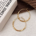 Macro detail of gold hoop earrings with small square beads on a textured knit background - Gold