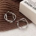 Detailed view of silver twisted geometric hoop earrings on textured knit background - Silver