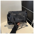 Close-up of black patent leather shoulder bag featuring silver chain and metal buckle - Black