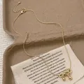 Eleganter vergoldeter Schleifen-Anhänger mit Schlangenkette auf Vintage-Stoffuntergrund - Gold