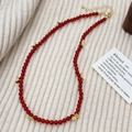 Detail van rode agaat kralenketting met gouden vlinderhangers op witte gebreide stof - Rode Agaat Vlinder Ketting