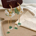 Detailed macro view of gold tassel earrings with green stone, pearl, and frosted flower - Green Crystal Flower Tassel Style / Green