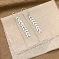 Detailed view of silver leaf tassel drop earrings on minimalist vintage fabric background - Silver