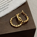 Close-up of golden geometric hoop earrings featuring beaded cube accents on wood surface - Gold